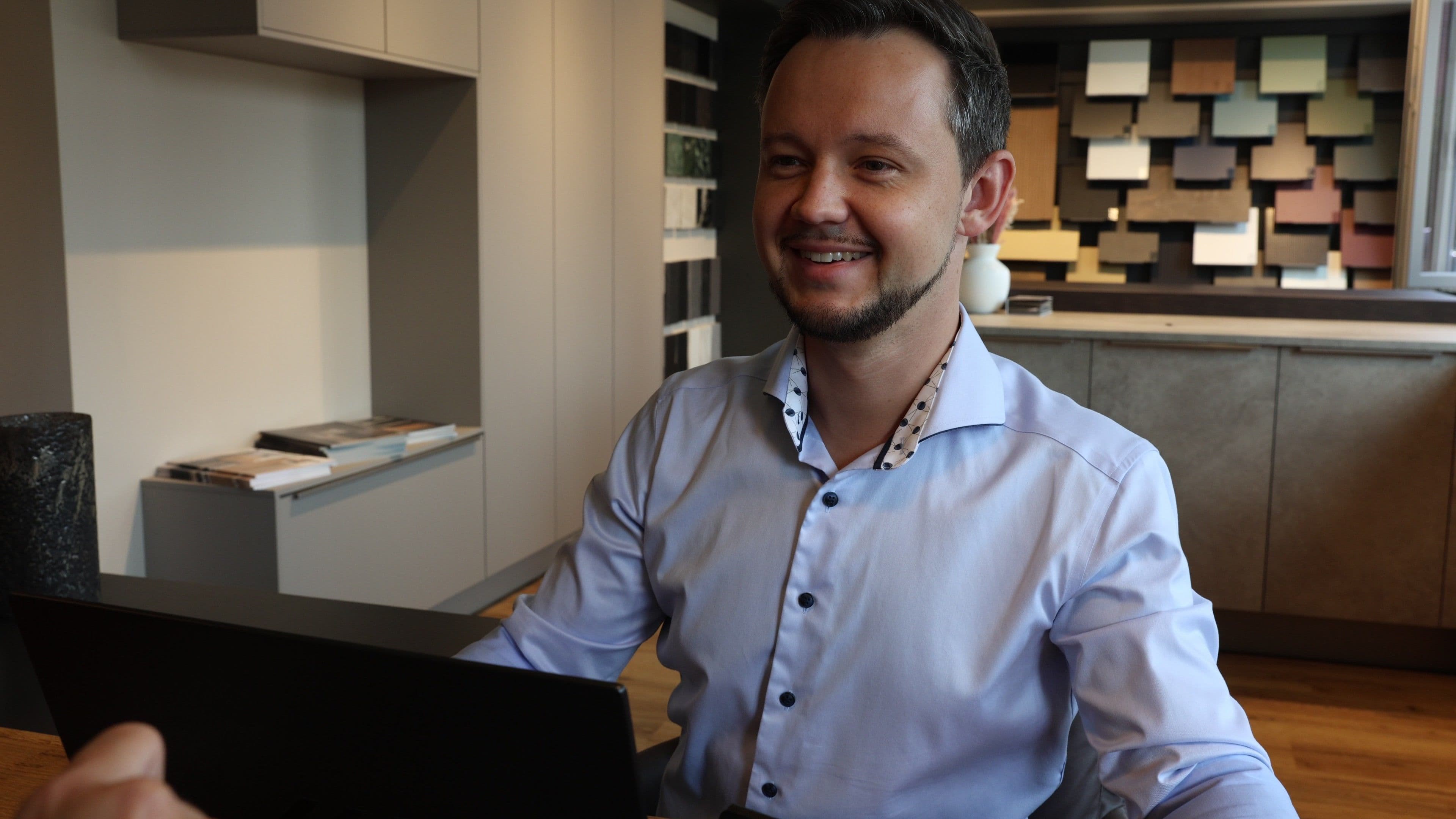 Thomas Kirschner berät eine Kundin am Holztisch im Thoki Studio Wörthsee, Material-Wand im Hintergrund, Laptop mit Planungs-Skizze