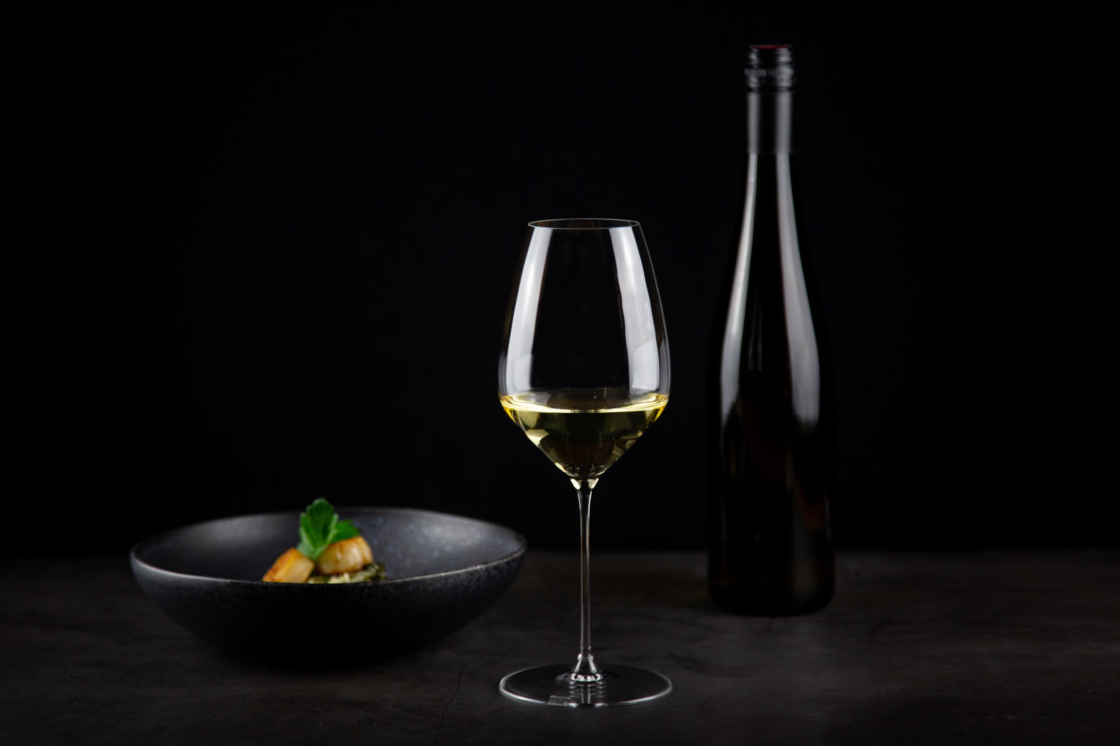 Riedel Riesling-Glas mit Weinflasche, Stillleben auf schwarzem Grund